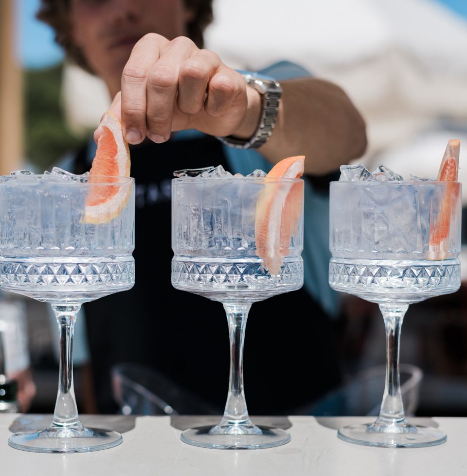 A bartender adds a segment of grapefruit to a cocktail glass