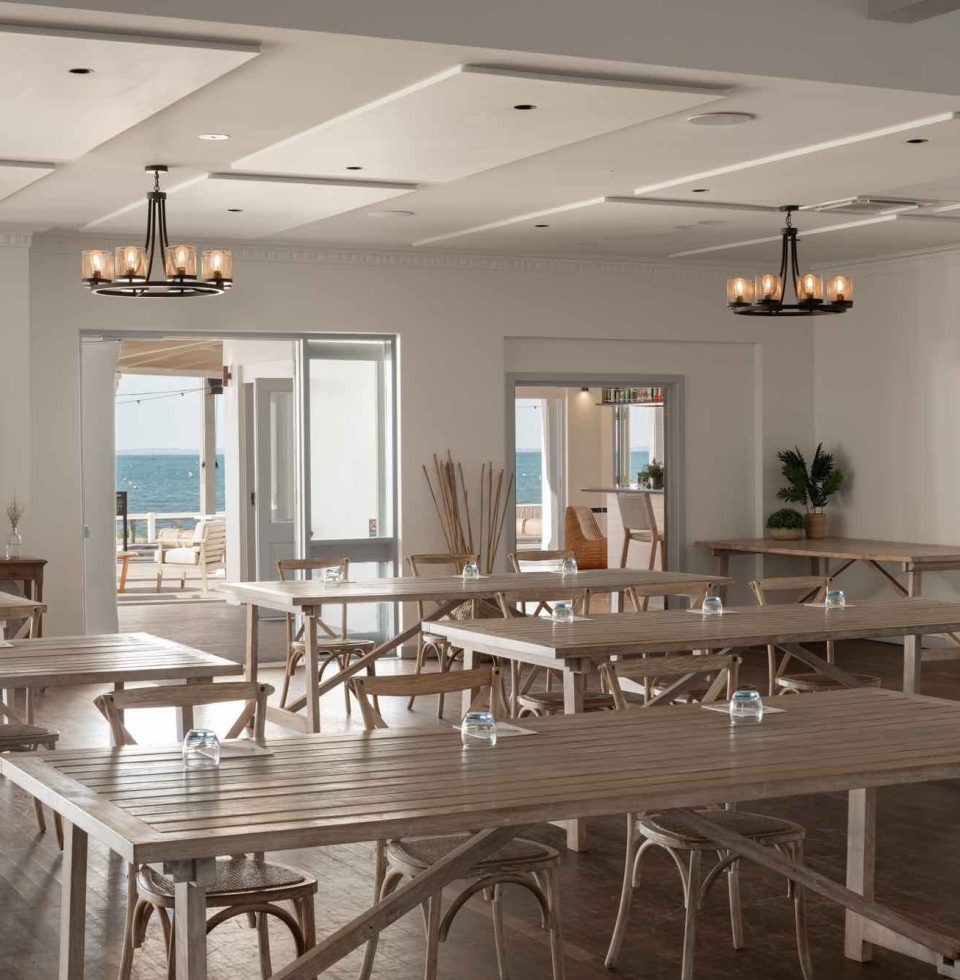function room with a range of wooden tables, wooden chairs, and chandeliers and a view of the ocean