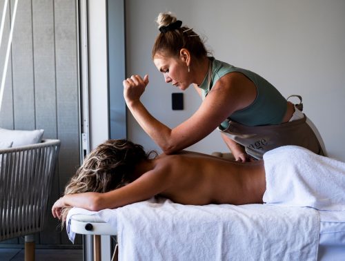 A masseuse leans her elbow in between a guest's shoulder blades during a massage session