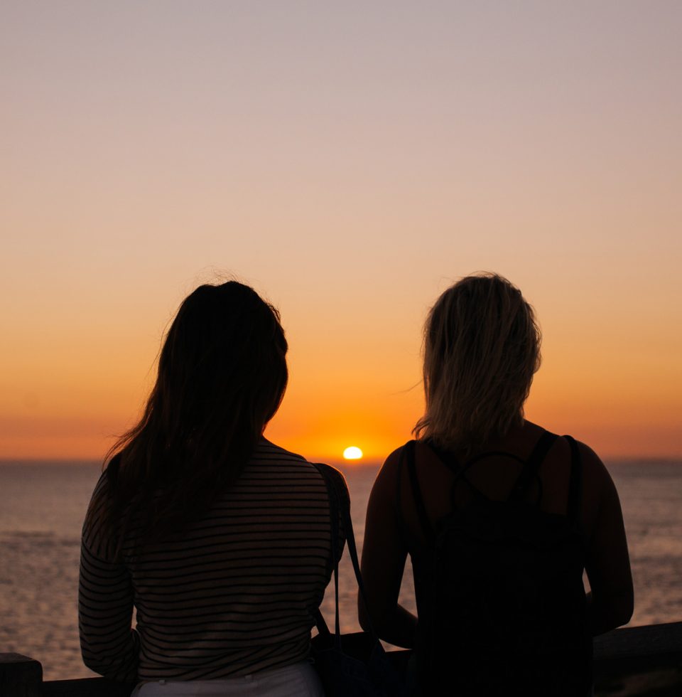 Two tourists watch a sunset over the water