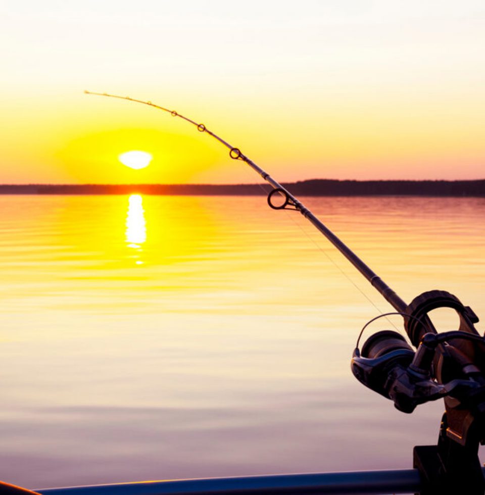 A fishing rod is cast over the ocean while the sun goes down