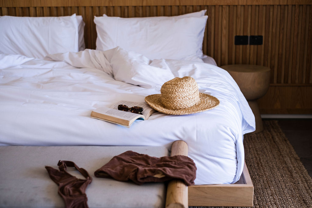 A hat, book, and pair of sunglasses sit atop a hotel bed