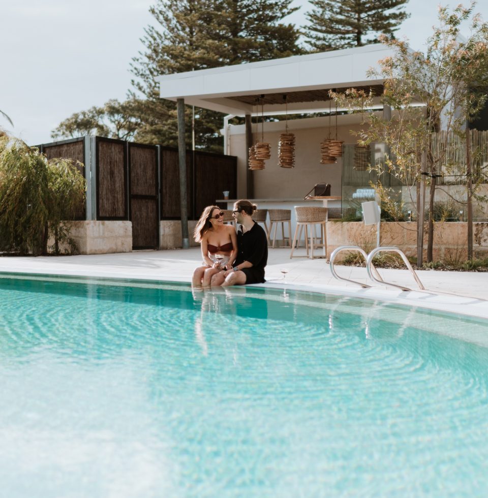 Two Samphire Rottnest guests dip their feet in the hotel pool while enjoying a drink