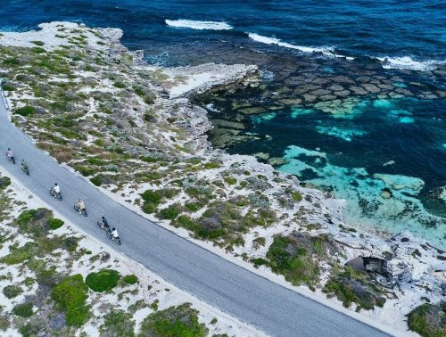 Tourists ride bikes down a path with the Rottnest ocean in the background