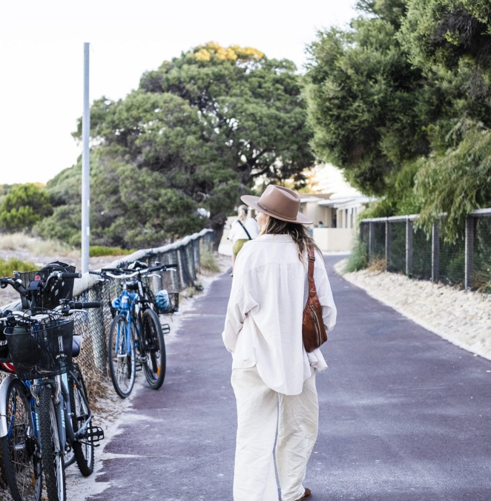 Tourist walks down the front on Rottnest Island, beside some bikes stacked up against the fence